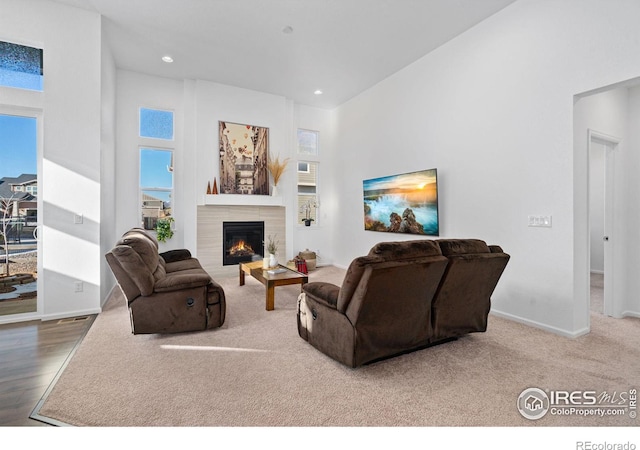 living room with a high ceiling, recessed lighting, a glass covered fireplace, and baseboards