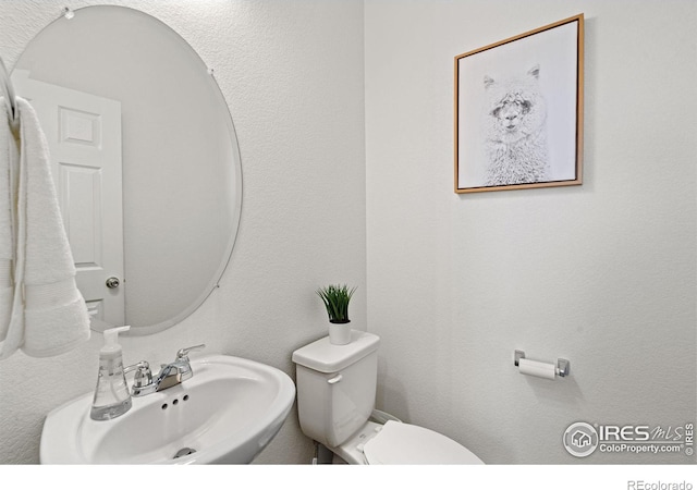 bathroom with a textured wall, a sink, and toilet