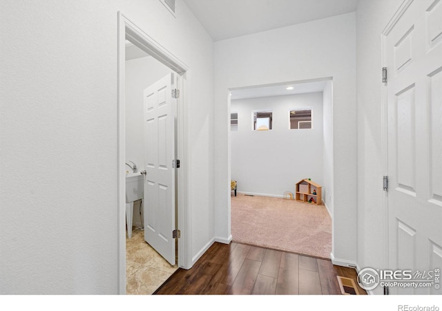 hallway featuring visible vents, baseboards, and wood finished floors