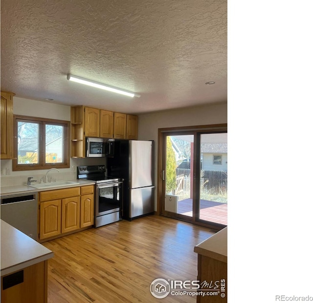 kitchen with stainless steel appliances, a sink, light countertops, light wood-type flooring, and open shelves