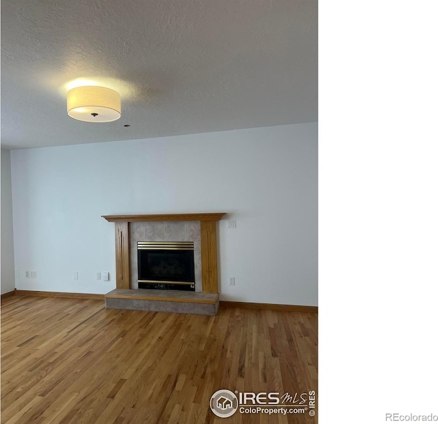 unfurnished living room with a textured ceiling, baseboards, wood finished floors, and a tile fireplace