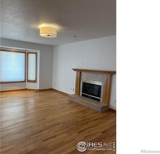 unfurnished living room featuring a textured ceiling, a fireplace, wood finished floors, and baseboards