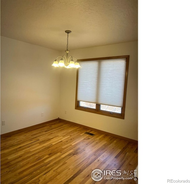 unfurnished room featuring a textured ceiling, wood finished floors, visible vents, baseboards, and an inviting chandelier