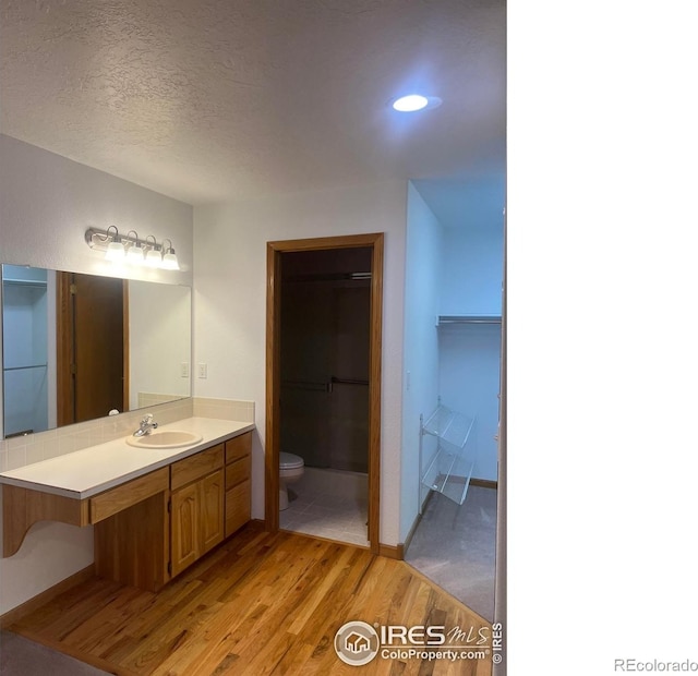 bathroom with a textured ceiling, toilet, wood finished floors, vanity, and a walk in closet