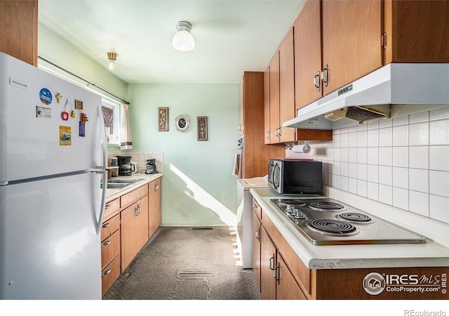 kitchen with under cabinet range hood, light countertops, freestanding refrigerator, stovetop, and stainless steel microwave