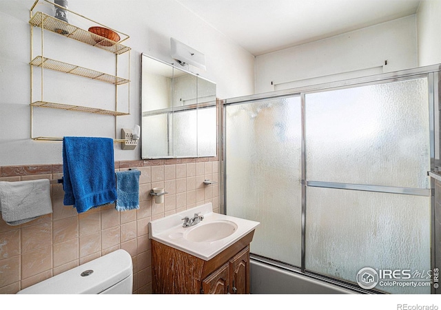 bathroom featuring tile walls, enclosed tub / shower combo, vanity, and toilet