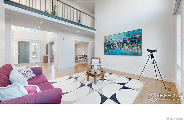 living room with a high ceiling, recessed lighting, wood finished floors, and baseboards