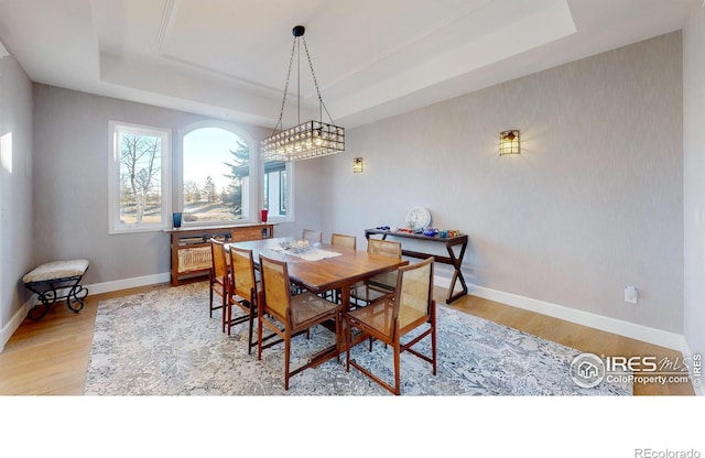 dining area featuring light wood-type flooring, baseboards, and a raised ceiling