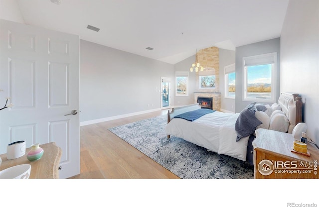 bedroom featuring visible vents, baseboards, lofted ceiling, wood finished floors, and a stone fireplace