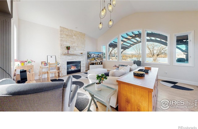 living room featuring lofted ceiling, a stone fireplace, baseboards, and wood finished floors