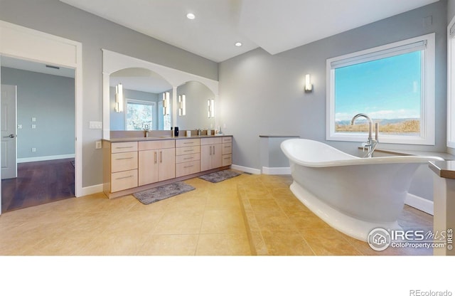 bathroom featuring recessed lighting, a sink, baseboards, a soaking tub, and double vanity