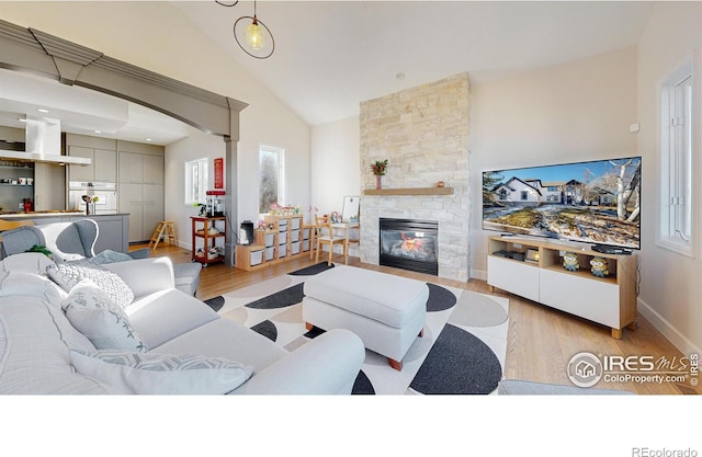 living room featuring high vaulted ceiling, a fireplace, baseboards, and wood finished floors