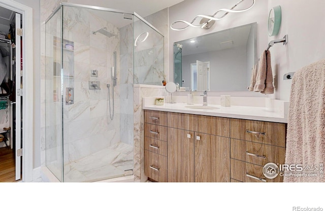 bathroom featuring a walk in closet, vanity, and a marble finish shower