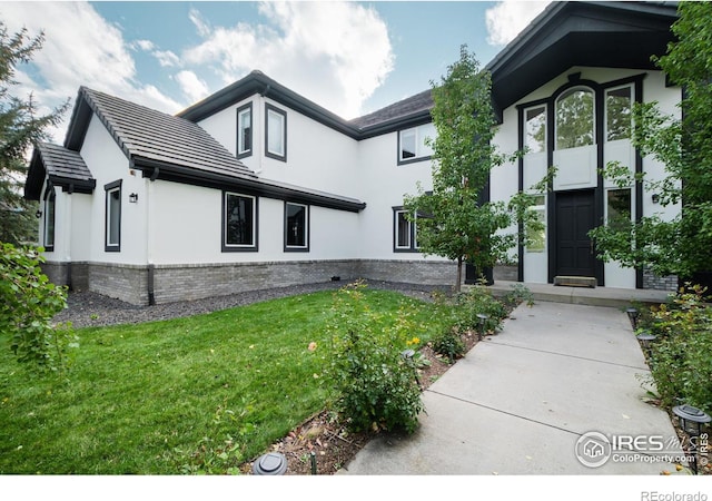 exterior space with a front yard, brick siding, and stucco siding