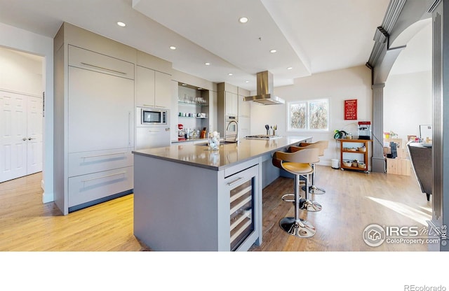 kitchen with beverage cooler, light wood-style floors, appliances with stainless steel finishes, island exhaust hood, and a center island with sink