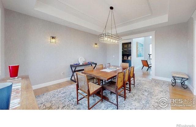 dining space with a raised ceiling, baseboards, and wood finished floors