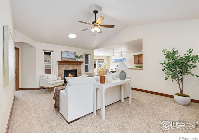 living room featuring lofted ceiling, a ceiling fan, a high end fireplace, light carpet, and baseboards