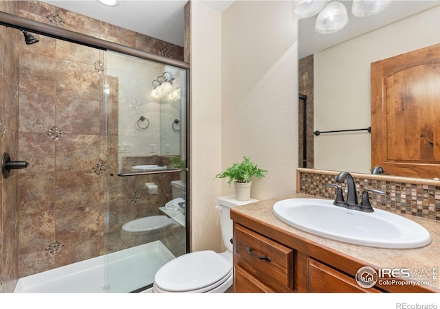 bathroom featuring vanity, backsplash, a shower stall, and toilet