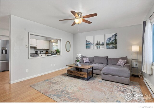 living room with light wood-style floors, a baseboard heating unit, ceiling fan, and baseboards