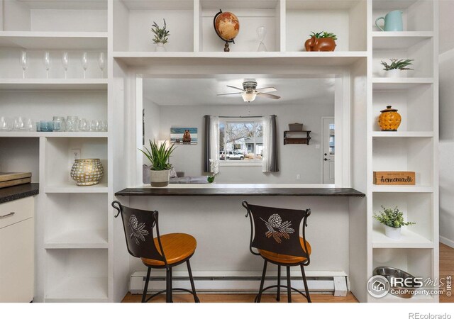 kitchen with open shelves, baseboard heating, a ceiling fan, and a kitchen breakfast bar