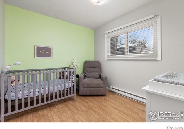 bedroom featuring light wood-type flooring, a nursery area, and a baseboard heating unit