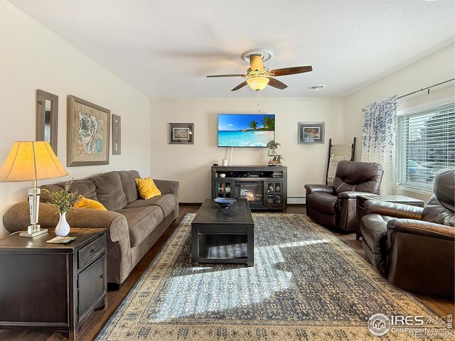 living area with a baseboard radiator, visible vents, dark wood finished floors, and ceiling fan