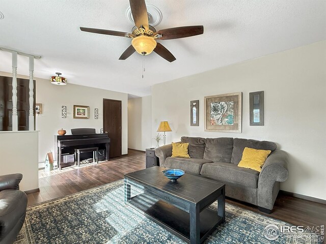 living room featuring a ceiling fan, dark wood-style flooring, a textured ceiling, and baseboards