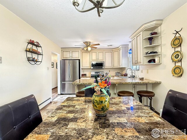 kitchen featuring stone countertops, a peninsula, cream cabinets, stainless steel appliances, and a kitchen bar