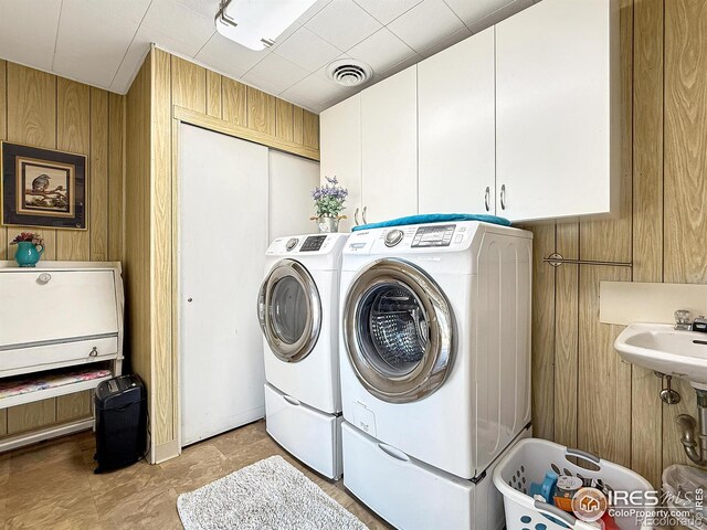 washroom featuring cabinet space, visible vents, wood walls, a sink, and independent washer and dryer