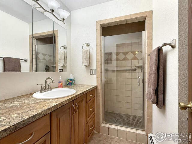 full bathroom with a textured wall, baseboard heating, a shower stall, vanity, and tile patterned flooring