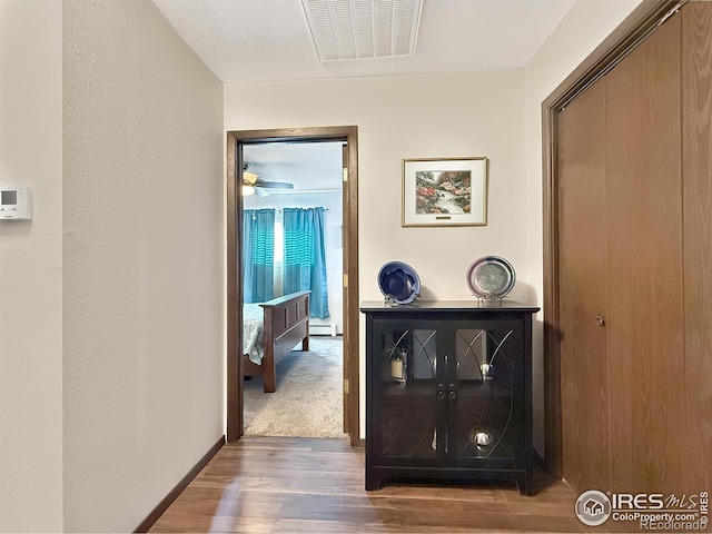 corridor with a baseboard radiator, dark wood finished floors, visible vents, and baseboards