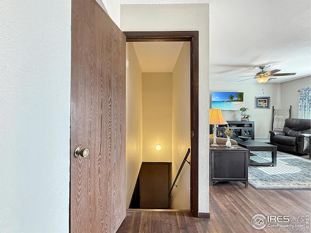 stairs featuring ceiling fan, a textured wall, baseboards, and wood finished floors