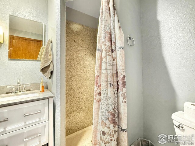 full bathroom with toilet, a textured wall, a shower stall, and vanity