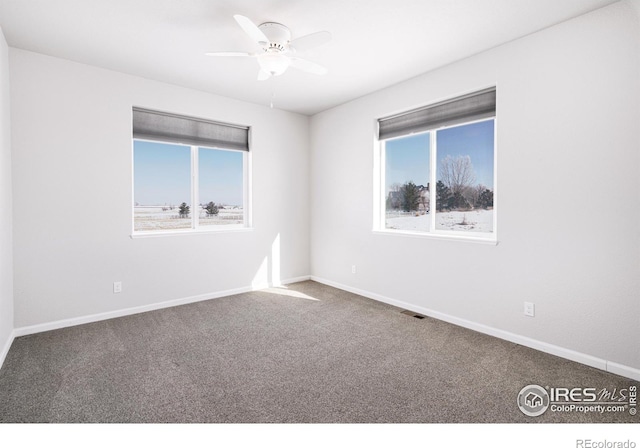 carpeted spare room with a ceiling fan, plenty of natural light, visible vents, and baseboards