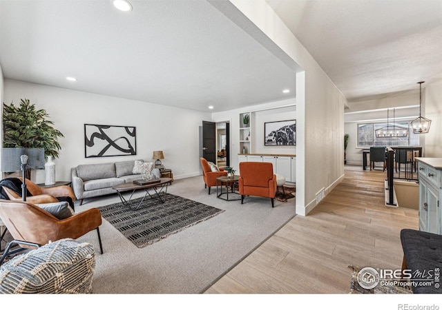 living room featuring baseboards, recessed lighting, light wood-type flooring, and an inviting chandelier