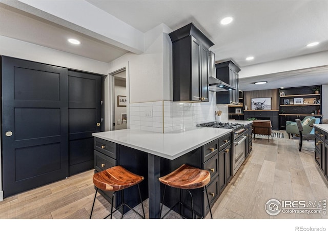 kitchen with light wood finished floors, tasteful backsplash, stainless steel range, a breakfast bar area, and light countertops