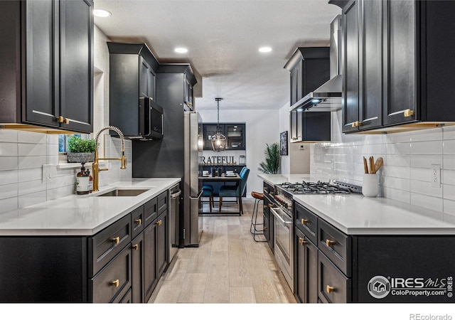 kitchen featuring stainless steel appliances, light countertops, light wood-style flooring, a sink, and wall chimney exhaust hood