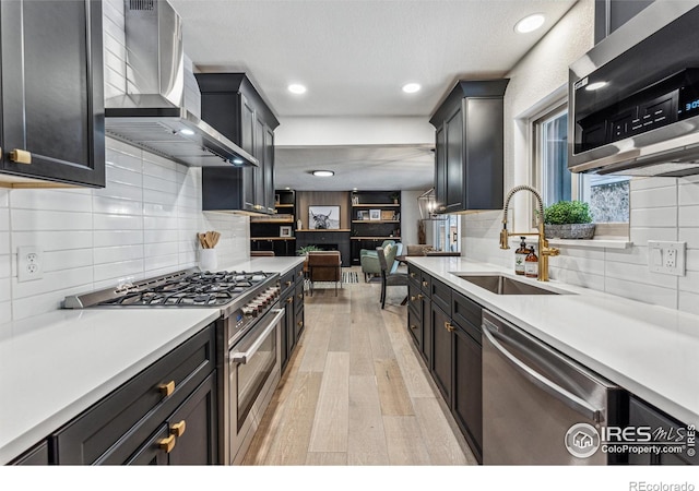 kitchen featuring wall chimney range hood, stainless steel appliances, a sink, and light countertops