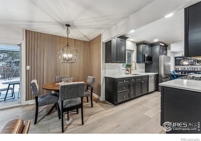 kitchen with stainless steel appliances, a sink, light countertops, decorative backsplash, and light wood finished floors