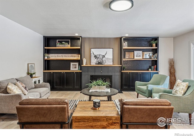 living area featuring a textured ceiling, built in shelves, a tile fireplace, and light wood-style flooring