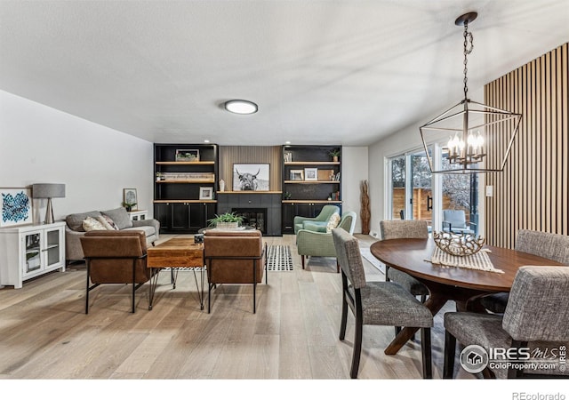 dining area with a tiled fireplace, a textured ceiling, light wood-type flooring, and a notable chandelier