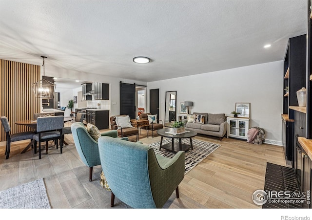 living area featuring a textured ceiling, a barn door, light wood-style flooring, and a notable chandelier