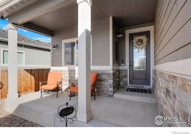 doorway to property with stone siding, covered porch, and fence