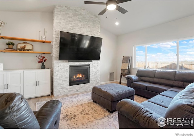 living area with lofted ceiling, a stone fireplace, wood finished floors, a ceiling fan, and baseboards