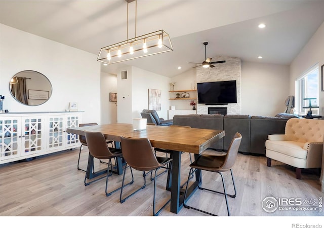 dining space with a large fireplace, visible vents, a ceiling fan, lofted ceiling, and light wood-type flooring