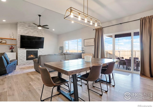 dining area with light wood-style floors, ceiling fan, a fireplace, and vaulted ceiling