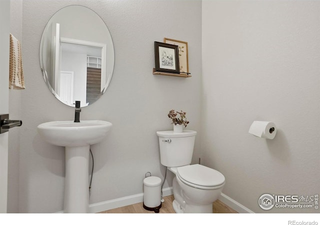 half bathroom with toilet, baseboards, and wood finished floors