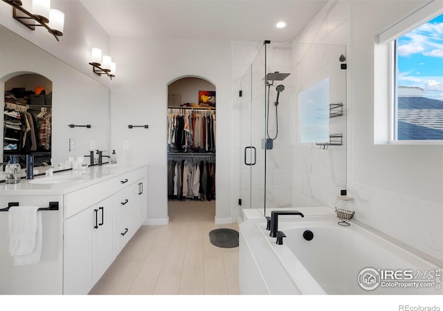 full bathroom featuring a walk in closet, double vanity, a stall shower, a sink, and a bath