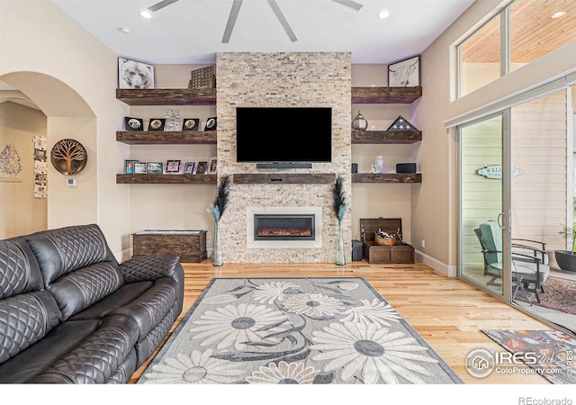 living room with built in features, arched walkways, recessed lighting, a stone fireplace, and wood finished floors