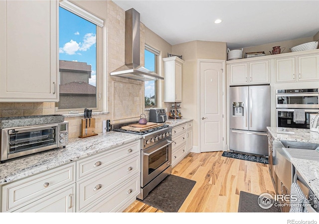 kitchen with backsplash, appliances with stainless steel finishes, light wood-style floors, white cabinets, and wall chimney exhaust hood